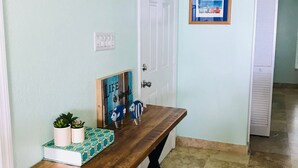 A hallway with a wooden bench, a door, a framed picture, and a small plant on the wall.