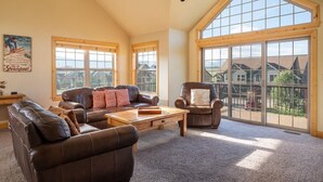 A spacious living room with a high ceiling, large windows, and a view of the neighborhood. - 67 Fireweed | 4BR Hot Tub, Sleeps 13 (Tabernash)