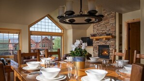 A dining room with a long wooden table set for a meal, a fireplace, and a large window overlooking a scenic view. - 67 Fireweed | 4BR Hot Tub, Sleeps 13 (Tabernash)
