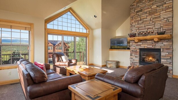 A living room with a fireplace, leather sofas, wooden coffee table, and large windows. - 67 Fireweed | 4BR Hot Tub, Sleeps 13 (Tabernash)
