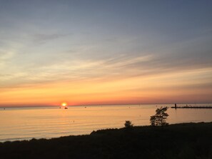 A sunset over a calm body of water with a distant pier and a few boats.