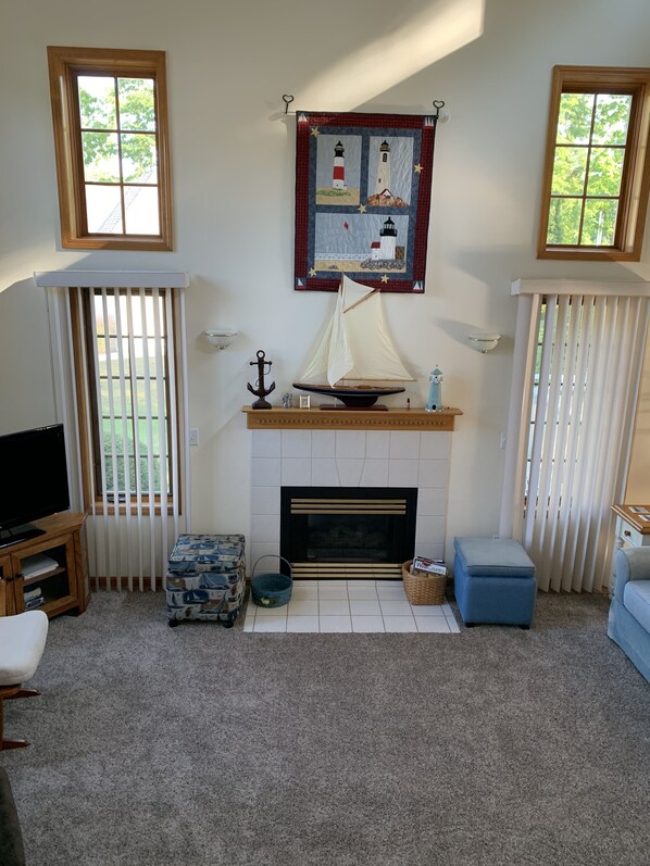A living room with a fireplace, a sailboat model, and a lighthouse quilt.