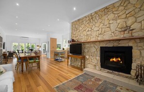 A spacious living room with a stone wall fireplace, wooden flooring, and a dining area with a table and chairs. - ROSE COTTAGE SORRENTO | WALK TO BEACH & VILLAGE | FAMILY & COUPLES ESCAPE (Sorrento)