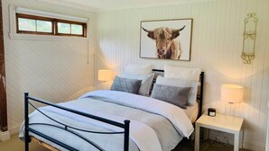Ein Schlafzimmer mit einem Bett, Nachttischlampen, einem gerahmten Bild an der Wand und einem Fenster mit Jalousien.