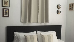 Un letto con biancheria da letto bianca e due cuscini, una testiera scura e una tenda beige.
