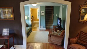 A living room with a wooden floor, a sofa, a chair, a TV, and a staircase leading to another room. - Maple View House, 3 fireplaces, sauna, game room, 4 living rooms, 4 TVs, grill (North Conway)