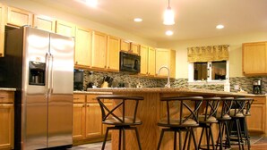 A modern kitchen with wooden cabinets, a stainless steel refrigerator, a microwave, and a bar area with stools. - Maple View House, 3 fireplaces, sauna, game room, 4 living rooms, 4 TVs, grill (North Conway)