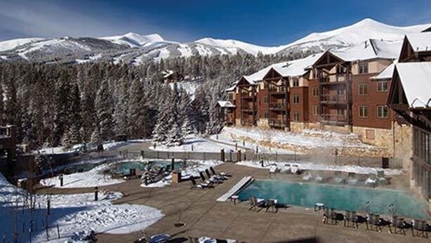 Een resort met een zwembad, skipistes en besneeuwde bergen.