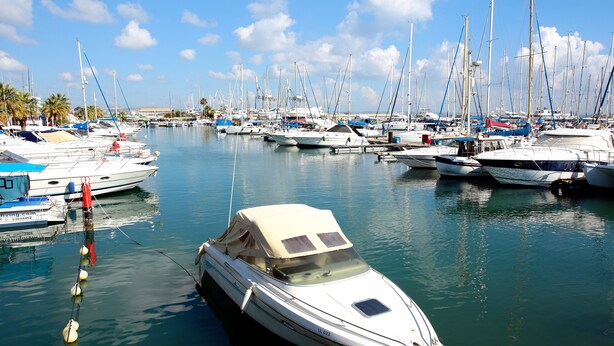 A marina with multiple boats docked, calm water, and a clear sky.