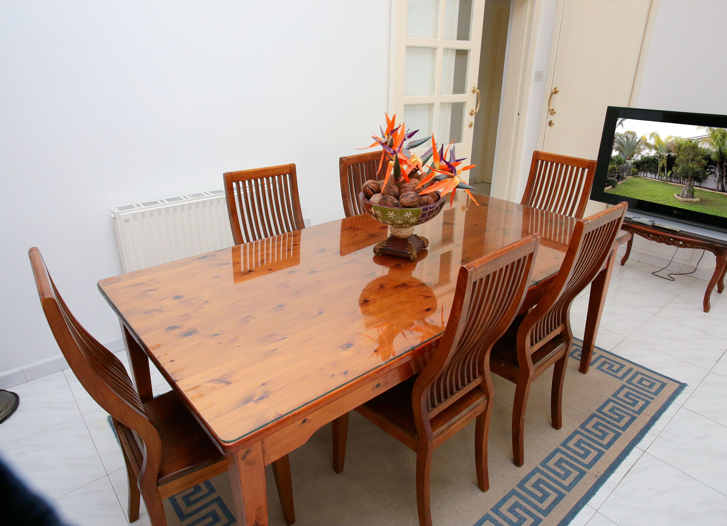 Un comedor con una mesa de madera, seis sillas, un cuenco decorativo y un televisor sobre un mueble bajo.
