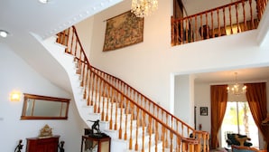 A grand staircase with wooden balusters, a chandelier, and a large painting on the wall.