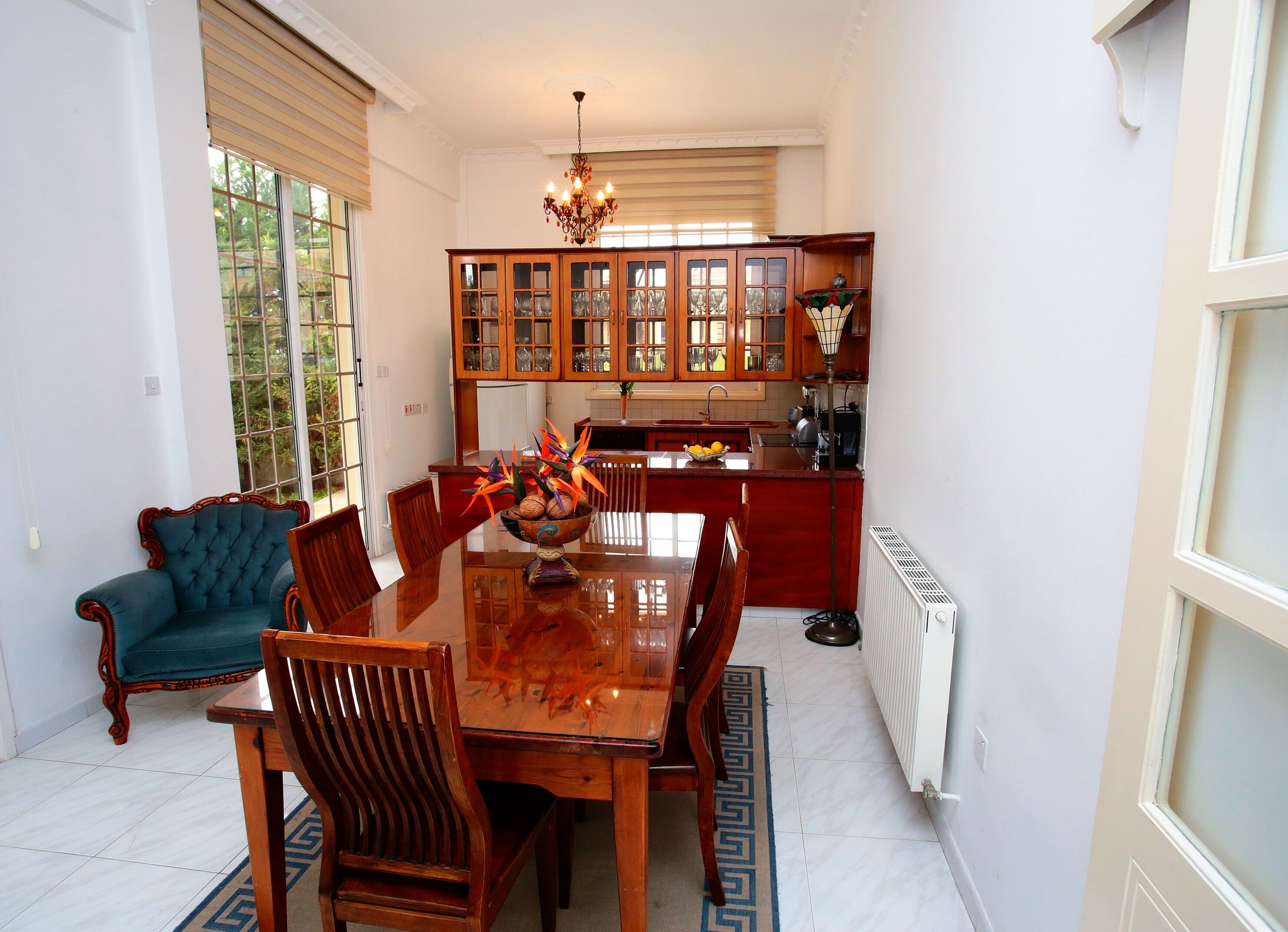 Un comedor con una mesa y sillas de madera, una araña y vistas a la cocina con armarios de madera.