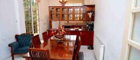 Un comedor con una mesa y sillas de madera, una araña y vistas a la cocina con armarios de madera.