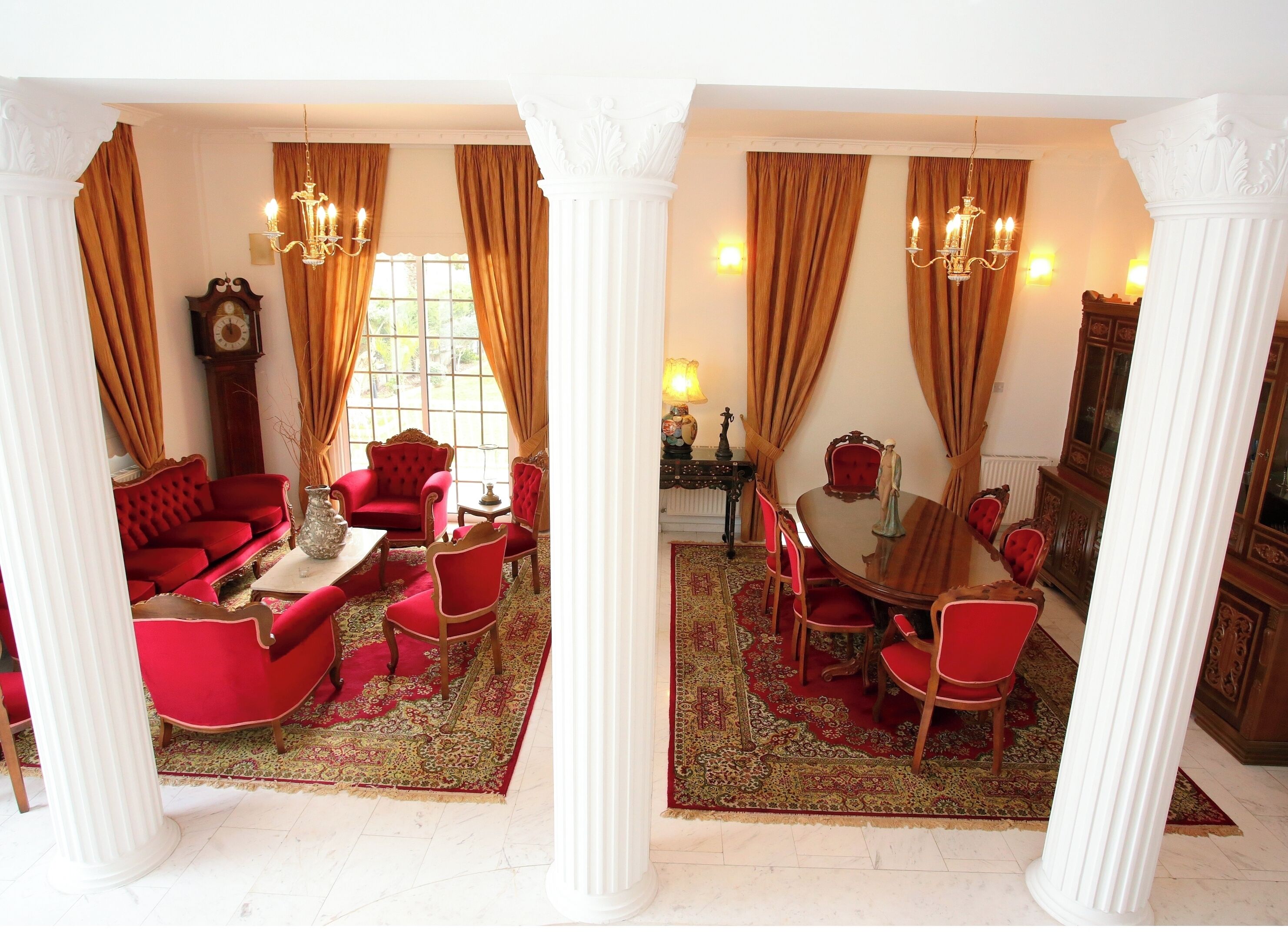 Une pièce comprenant un canapé rouge, une table à manger avec des chaises et un lustre.