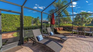 Área de estar coberta ao ar livre com espreguiçadeiras e um guarda-sol vermelho, com vista para um jardim paisagístico.