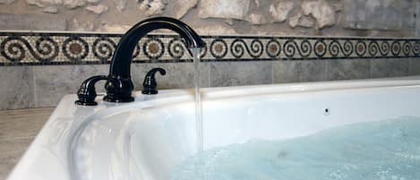 Una bañera con agua corriente, una pared de piedra y un borde decorativo de azulejos.