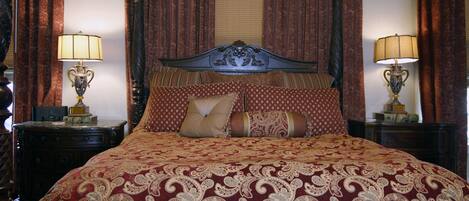 A large bed with a patterned bedspread, two bedside tables with lamps, and heavy drapery.