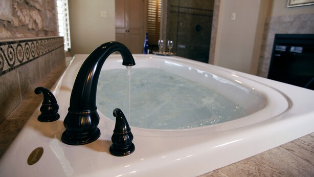 A bathroom with a white bathtub, black faucets, and a stone wall. - Legacy Suite on Main St in central downtown, jacuzzi tub, ask about Wine Tours!! (Fredericksburg)