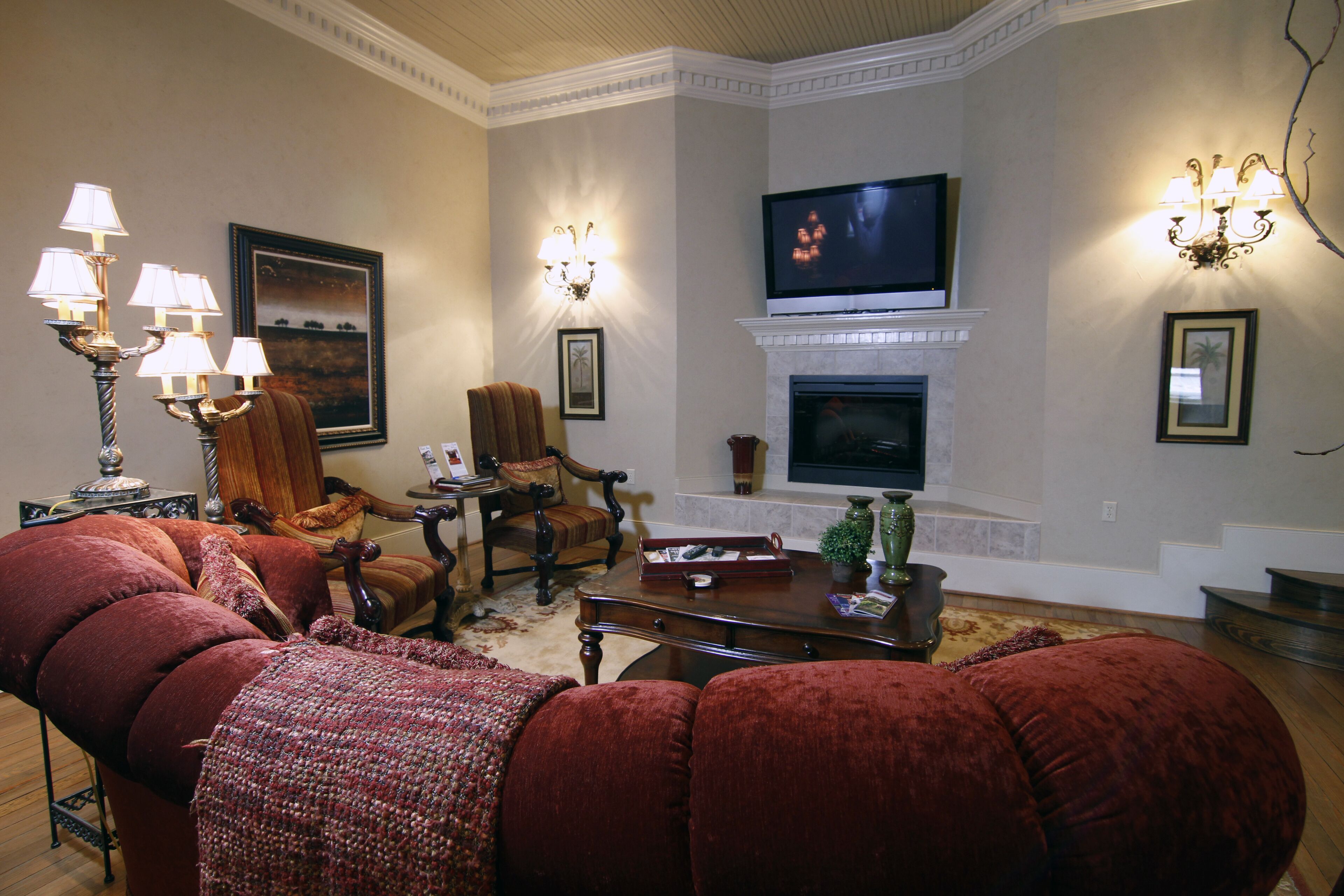 Ein Wohnzimmer mit Kamin, Fernseher und einer gemütlichen Sitzecke mit roten Sofas und Sesseln.