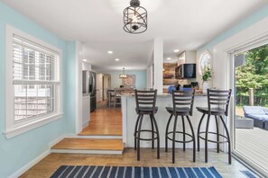 A modern kitchen with a bar area, wooden flooring, and a view of the outdoors. - Stellar Home with Hot Tub & Movie Room! (Chatham)