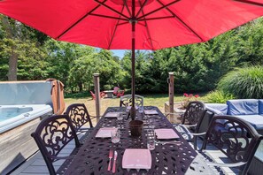 An outdoor dining area with a table set for two, a red umbrella, and a hot tub in the background.