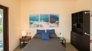 Un dormitorio con cama, dos mesitas de noche, una lámpara, una estantería y tres cuadros con motivos marinos en la pared.