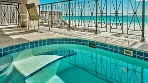 En swimmingpool med kristallklart blått vatten, omgiven av en kakelbeklädd poolterrass och ett metallräcke.