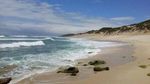 Une plage avec des vagues, des rochers et un ciel dégagé.