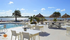 Un espace aménagé au bord de la piscine, avec des chaises longues, des tables et des parasols, donnant sur une étendue d’eau.