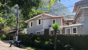 A residential street with a paved road, a parked motorcycle, and a house with a balcony. - House rental in Toque Toque Grande - São Sebastião (North Coast of SP) (São Sebastião)