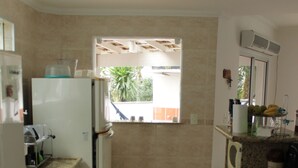 A compact kitchen with a refrigerator, microwave, stove, and a small window. - House rental in Toque Toque Grande - São Sebastião (North Coast of SP) (São Sebastião)