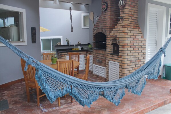 A hammock strung between chairs and a brick oven in a patio area.