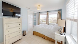 Un dormitorio con cama, cómoda, televisor y ventana con cortinas.