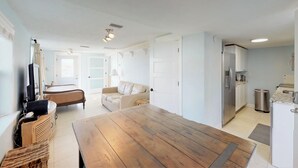 Una sala moderna con una mesa de comedor de madera, un sofá, un televisor y una zona de cocina con refrigerador y estufa.