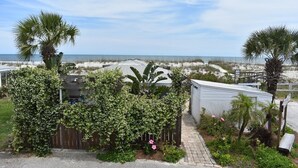 Una propiedad frente a la playa con una terraza de madera, un cobertizo pequeño y un jardín con plantas tropicales.