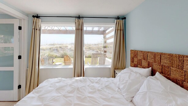 Un dormitorio con cama, cabecera de madera, ventana con cortinas y vistas al exterior.