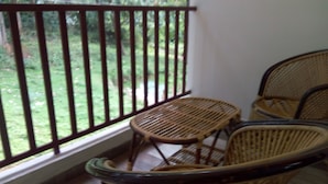 A balcony with wicker chairs, a view of a garden, and a white wall.