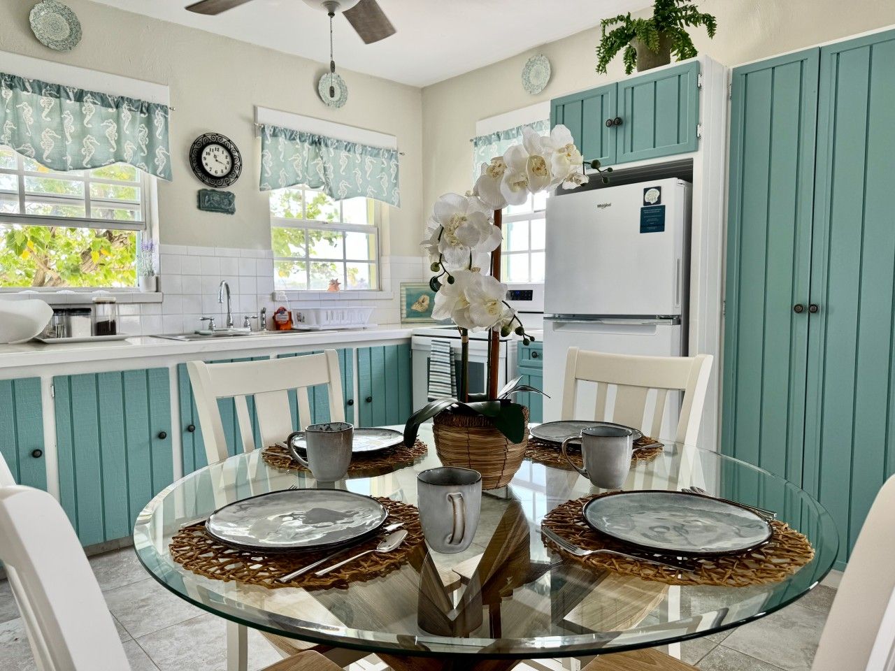 A kitchen with teal cabinets, a glass dining table, and a refrigerator.