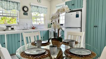 A kitchen with teal cabinets, a glass dining table, and a refrigerator.