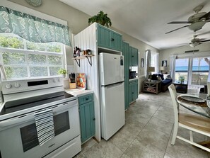Una cocina con horno empotrado, refrigerador y un comedor con mesa de vidrio y sillas.