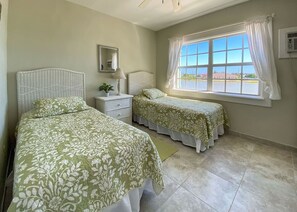 A bedroom with two beds, a nightstand, a mirror, and a window with curtains.