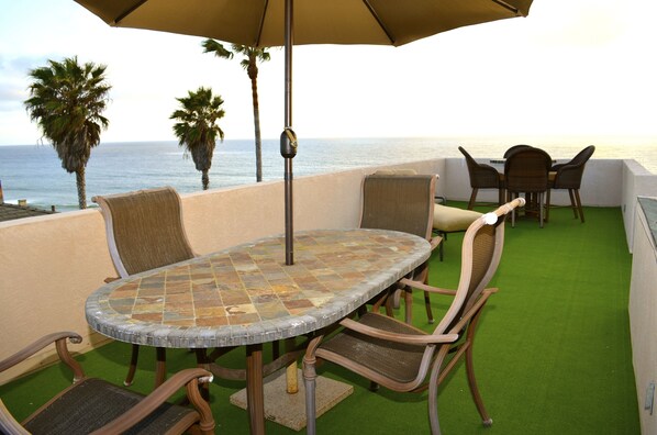 A round table with chairs and an umbrella, overlooking the ocean with palm trees in the background. - Charming I BR Apt Pacific Beach, Attached to Ocean Front Home. (San Diego)