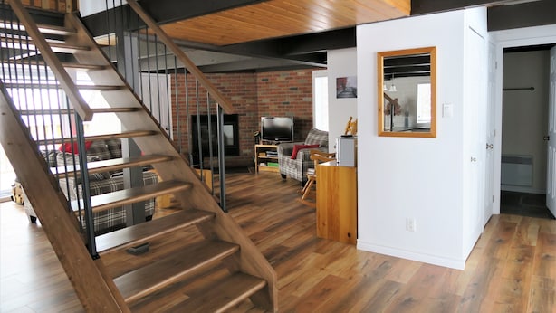Amplia sala de estar con una escalera de madera, pared de ladrillo y una cocina moderna.