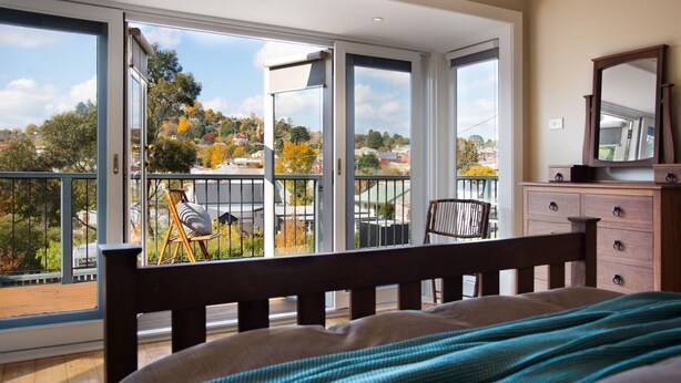 A bedroom with a bed, a dresser, a mirror, and a balcony with a chair and a table. - Jesmondene Daylesford (Daylesford)
