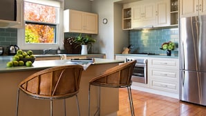 A modern kitchen with a central island, stainless steel appliances, and a view of autumn leaves through the window. - Jesmondene Daylesford (Daylesford)
