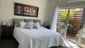 A bedroom with a bed, a nightstand, a painting, and a sliding glass door leading to an outdoor area.
