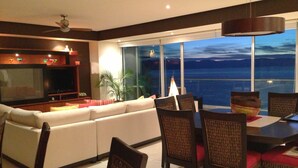 Una sala de estar moderna con un televisor grande, un sofá y una zona de comedor con sillas y una mesa.