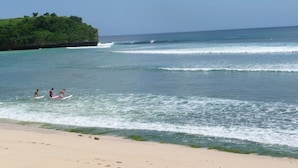 Une plage à l’eau d’un bleu limpide, avec un rivage sablonneux et une petite île verdoyante.