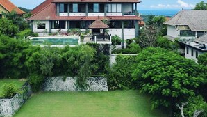 Une maison à deux étages avec une piscine, entourée d’une végétation luxuriante et offrant une vue dégagée sur l’océan.