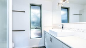 Une salle de bain moderne avec un grand miroir, des meubles blancs et une cabine de douche en verre.